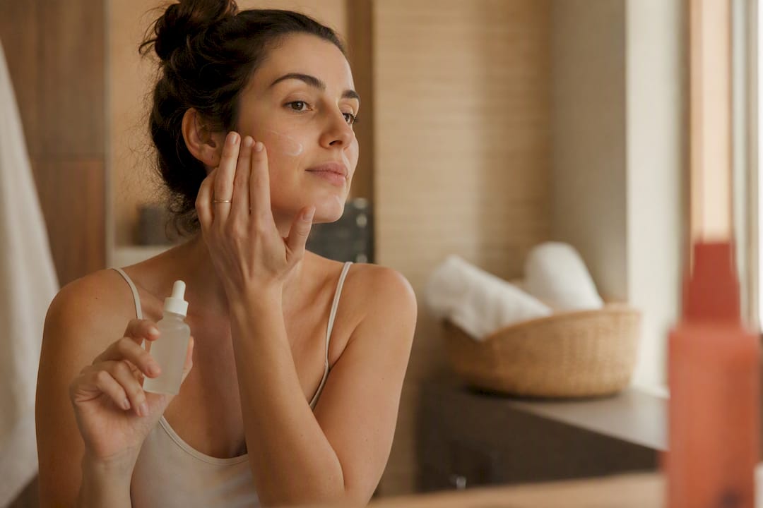 Μια γυναίκα απλώνει προσεκτικά serum στα μάγουλά της, φροντίζοντας το πρόσωπό της.